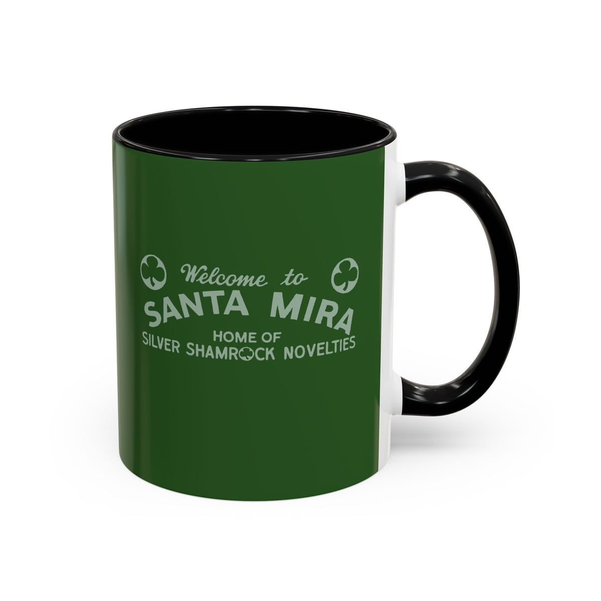 A ceramic coffee mug with a dark green exterior, black interior and handle, and white printed text reading 'Welcome to SANTA MIRA HOME OF SILVER SHAMROCK NOVELTIES' 
