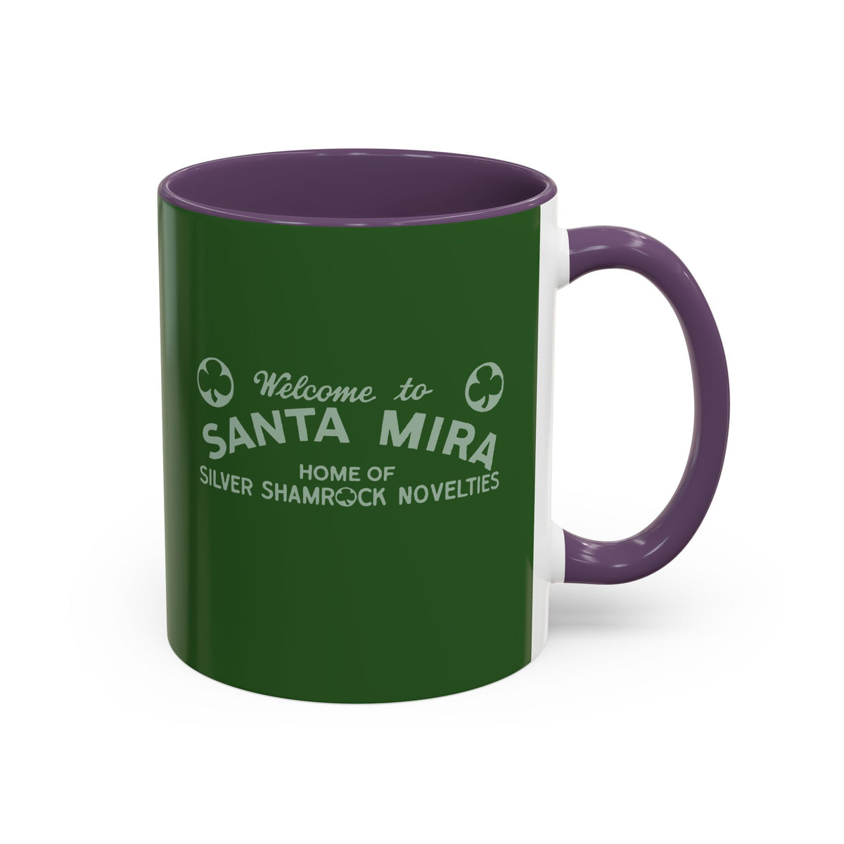 A ceramic mug with a dark green exterior, purple handle and interior, and white printed text reading 'Welcome to SANTA MIRA HOME OF SILVER SHAMROCK NOVELITIES' 