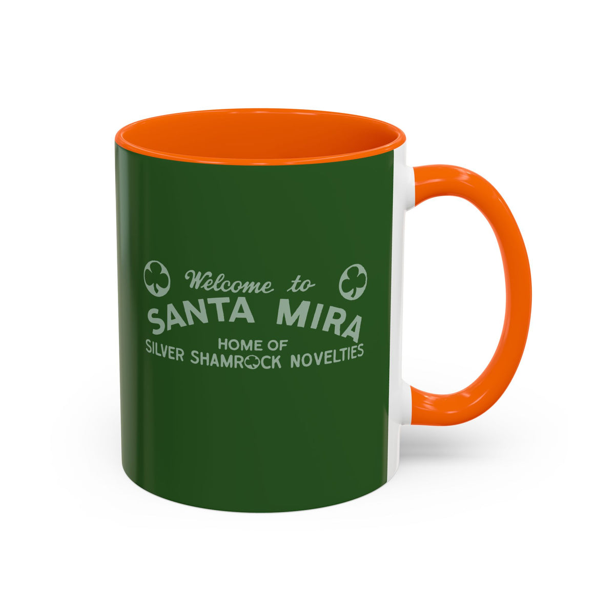 A ceramic mug with a dark green exterior, bright orange handle and interior, and white printed text reading 'Welcome to SANTA MIRA HOME OF SILVER SHAMROCK NOVELITIES' on a white background.