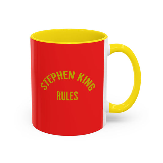 A ceramic mug with a bright red exterior, yellow interior and handle, featuring the text 'STEPHEN KING RULES' printed in yellow on the front.